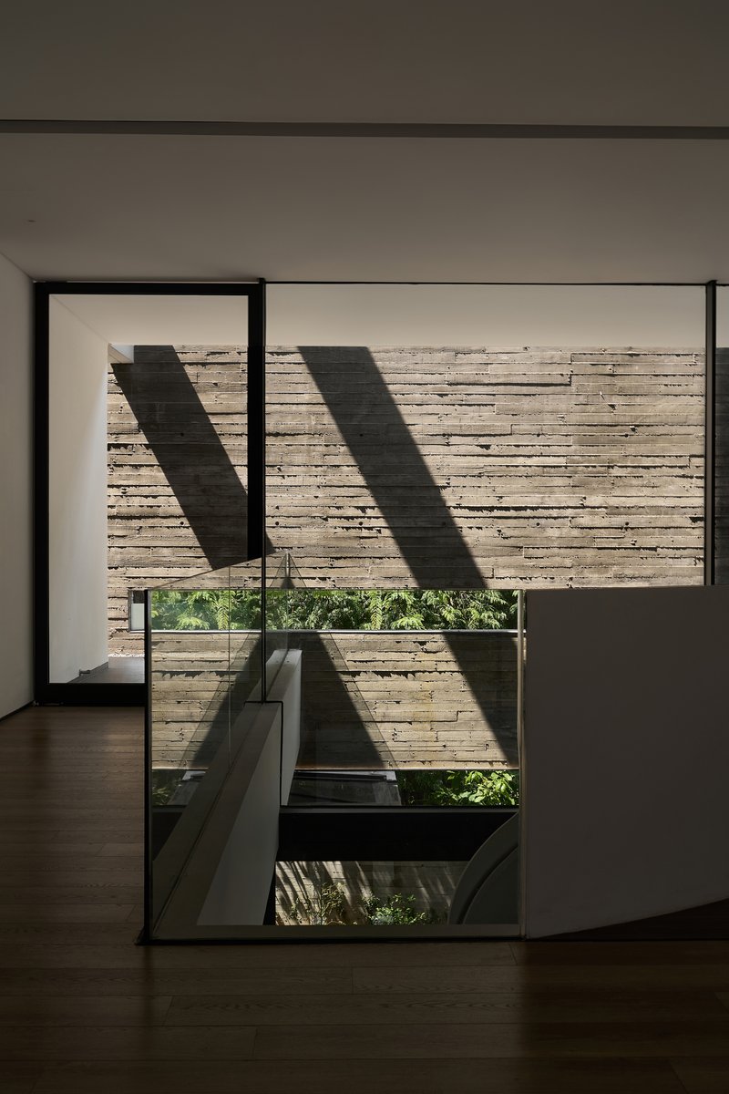 Floor-to-ceiling window framing a board-formed concrete wall with angular shadows from above