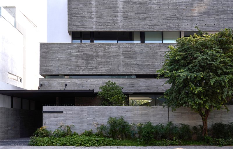 Entry facade showing layered concrete volumes with a cantilevered upper floor and planted foreground