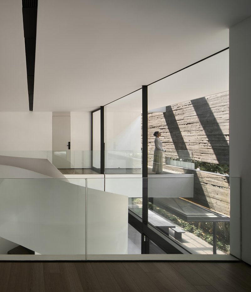 Interior hall with a figure walking past full-height glazing onto a courtyard terrace