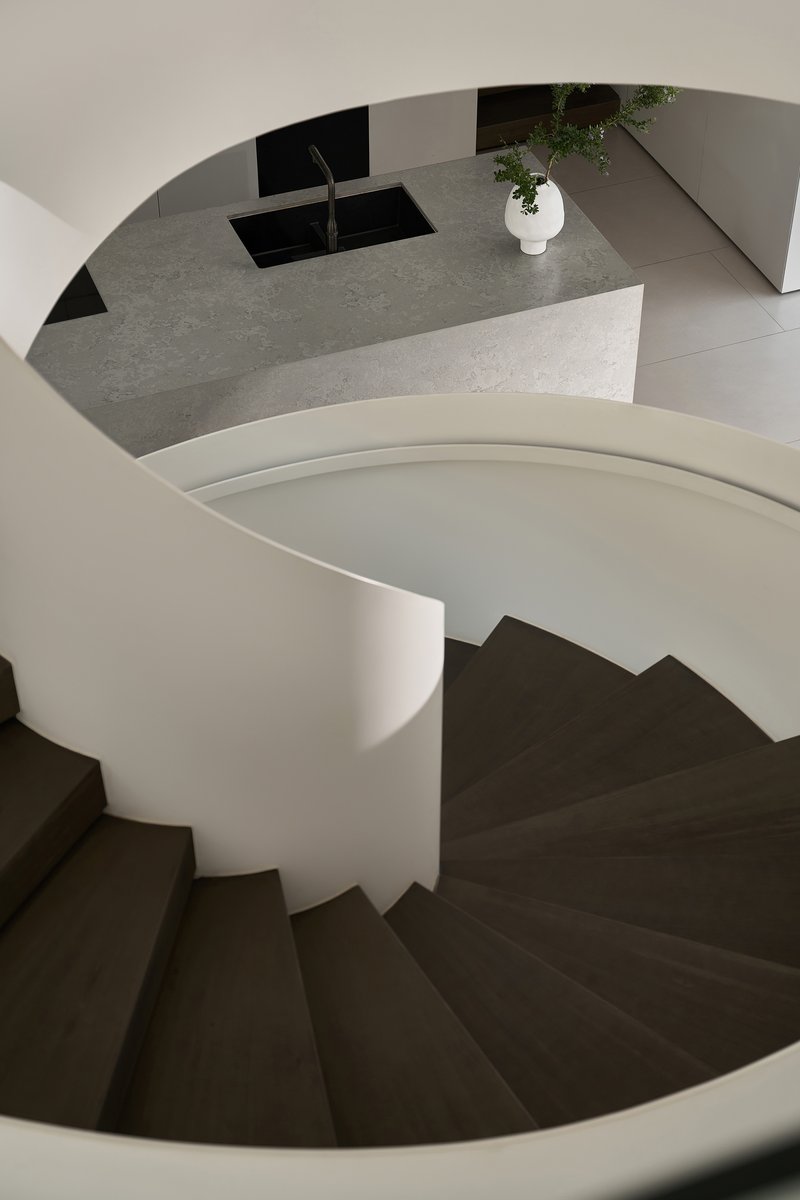 Top-down view of spiral staircase with dark treads and terrazzo island visible above