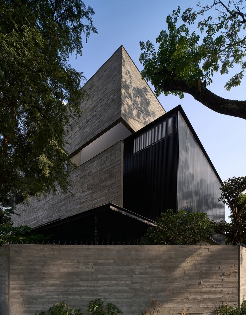 Stacked volumes clad in board-formed concrete and black metal beneath overhanging tree branches