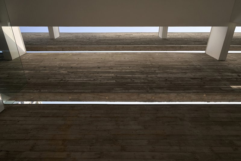 Upward view of timber bridge spanning between volumes under continuous skylight strips
