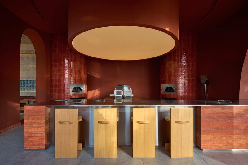 Counter with timber stools and stainless steel base beneath a circular ceiling recess in red-tiled interior