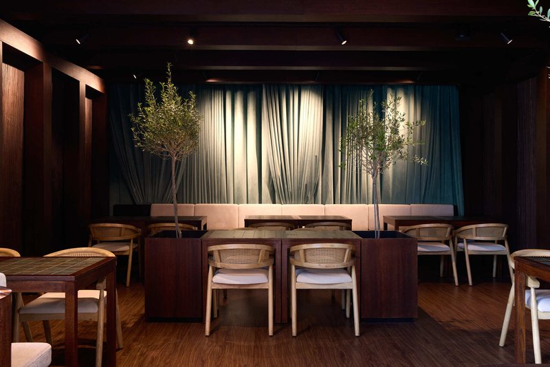 Dining area with dark timber paneling and cane-backed chairs beneath exposed ceiling beams and illuminated fabric drapes