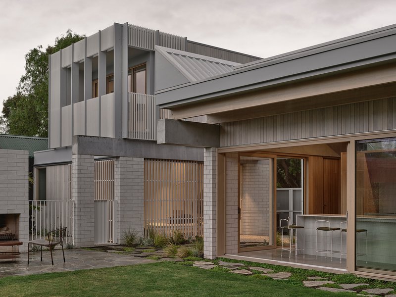 Rear courtyard showing the two-story corrugated metal volume above stacked brick walls at dusk