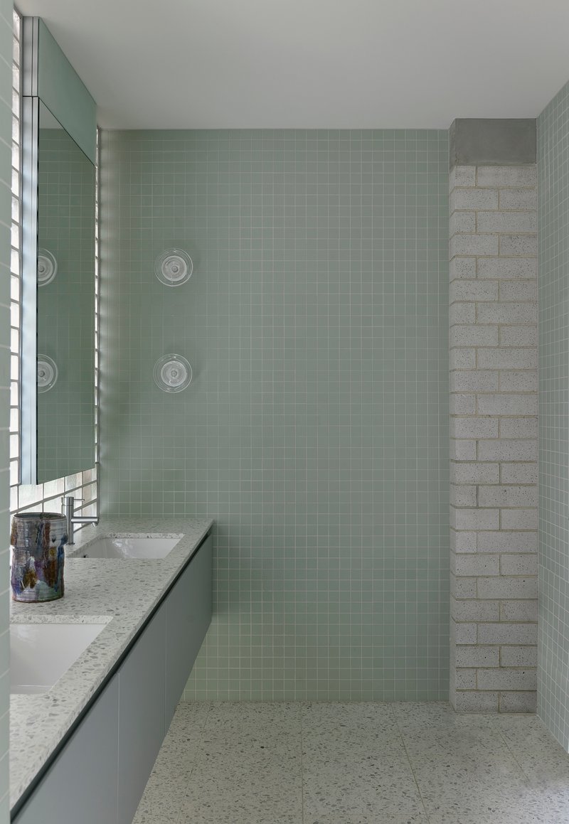 Shower area with sage green tile walls, rectangular glass block brick wall, and built-in wall fixtures