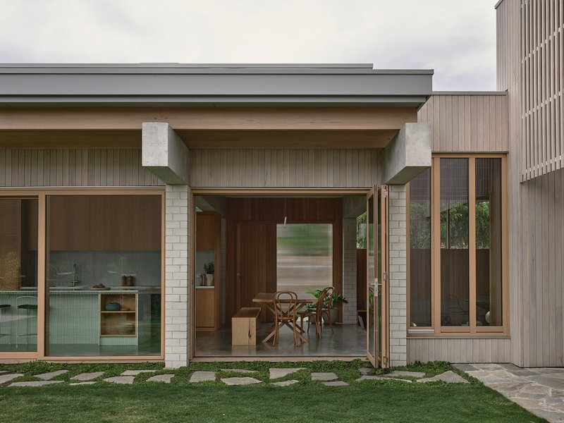Rear facade with concrete beams sheltering glazed openings and stone paver path through lawn