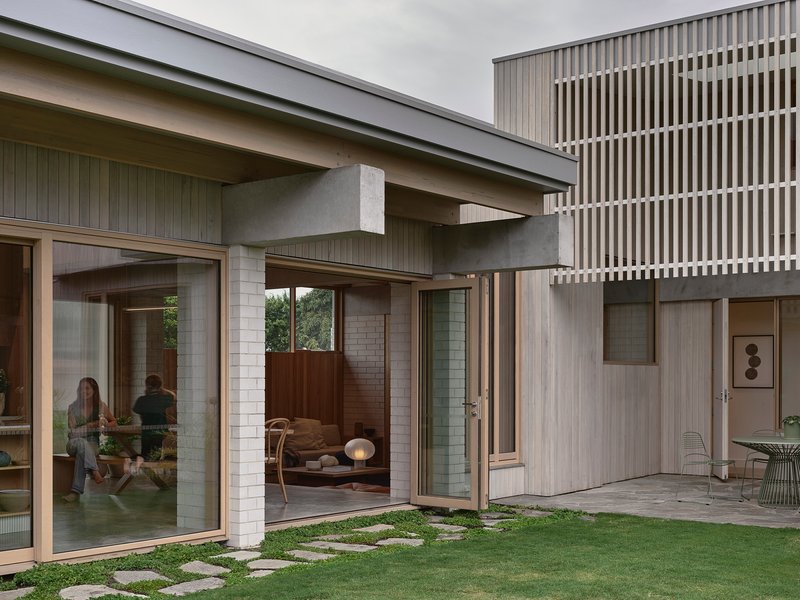 Glass-walled living area opening to a lawn courtyard with stepping stone path and residents inside