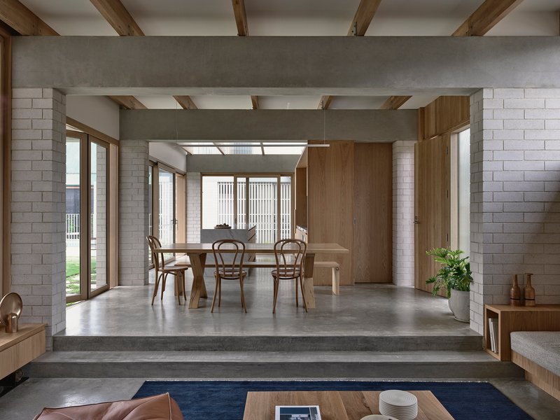 Dining area with timber table and chairs beneath exposed ceiling beams and vertical timber screen beyond