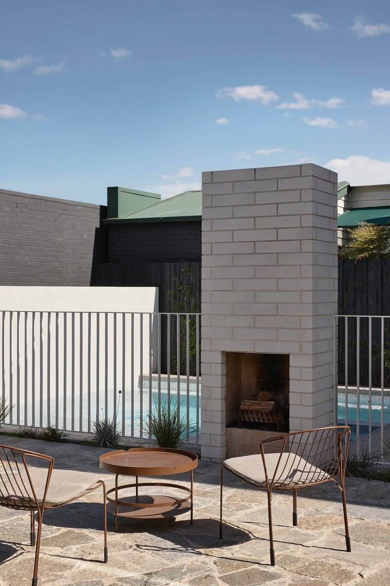 Outdoor concrete block fireplace with wire mesh chairs and round timber table beside the pool