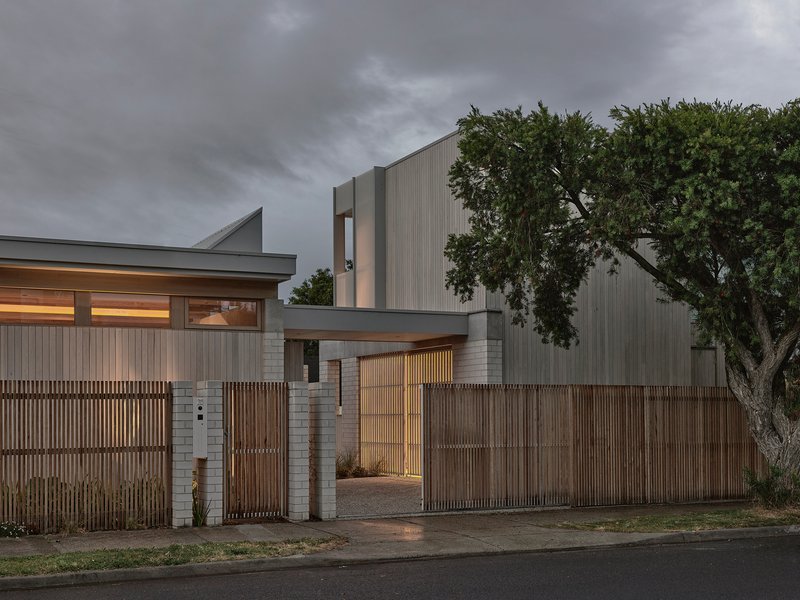 Entry courtyard with timber slatted gate and vertical screen fence beside an old tree at twilight