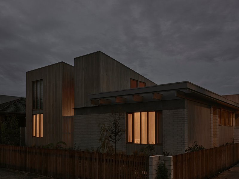 Street view of the timber-clad facade with vertical slatted windows glowing warmly at dusk
