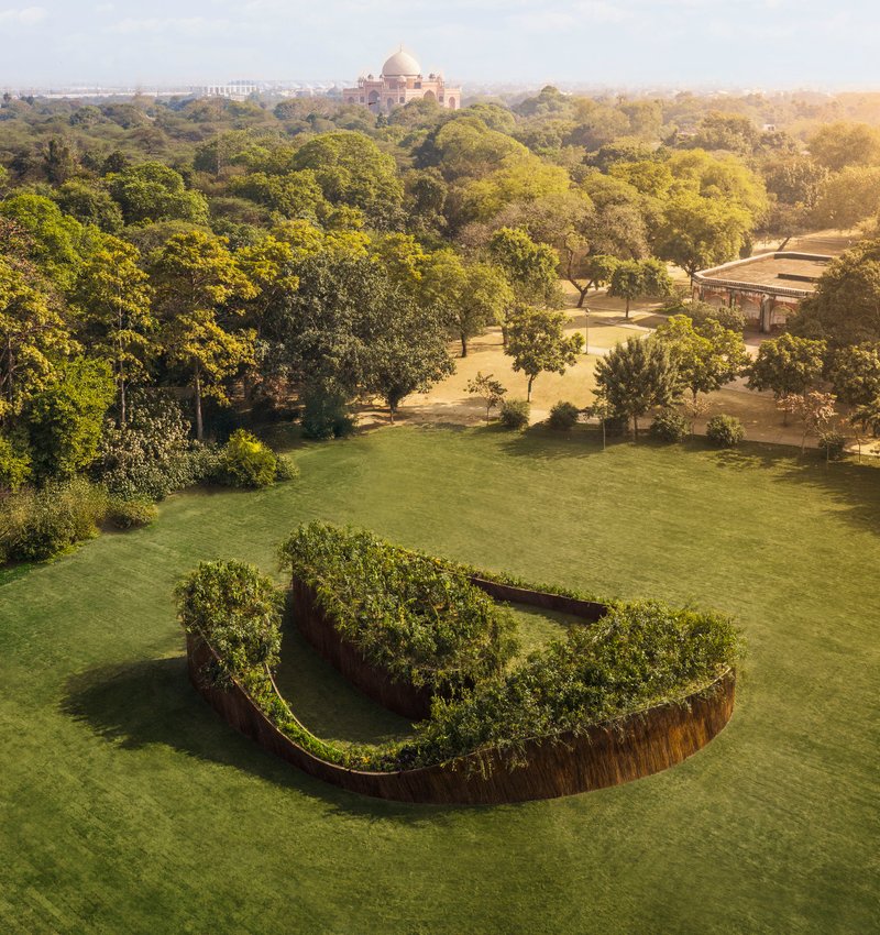 Aerial view of the spiral green-roofed structure in parkland with distant dome visible through haze