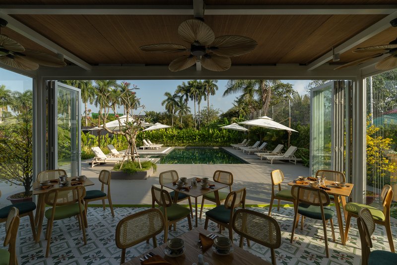 Open-air dining room with folding glass walls overlooking swimming pool surrounded by palm trees and loungers