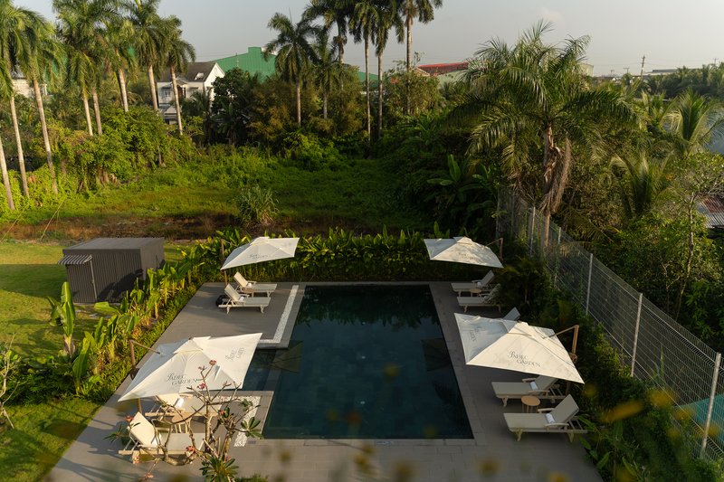 Elevated view of rectangular pool deck with white umbrellas set within lush tropical garden landscape