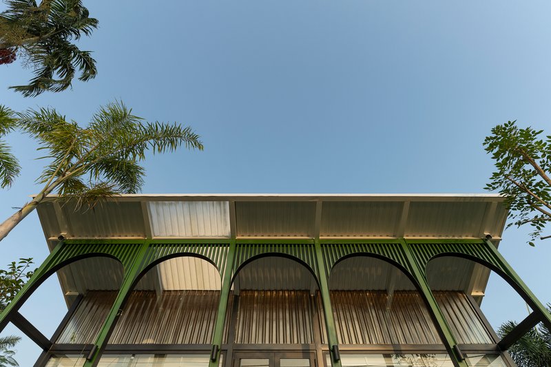 Upward view of the corrugated metal facade with green arched supports framed by palm fronds