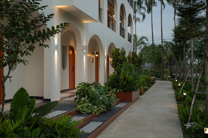 White arched facade with planted beds and concrete walkway at dusk under palm canopy