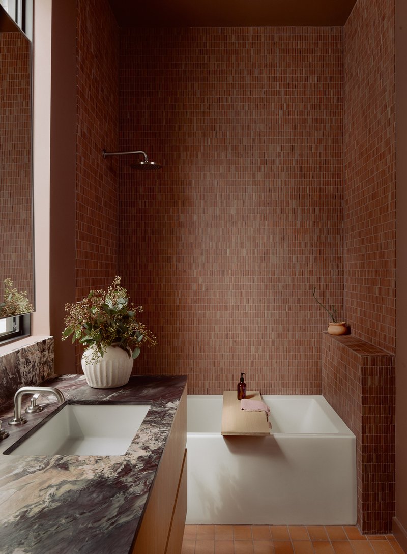 Bath alcove clad entirely in small brown mosaic tiles with freestanding tub and overhead shower
