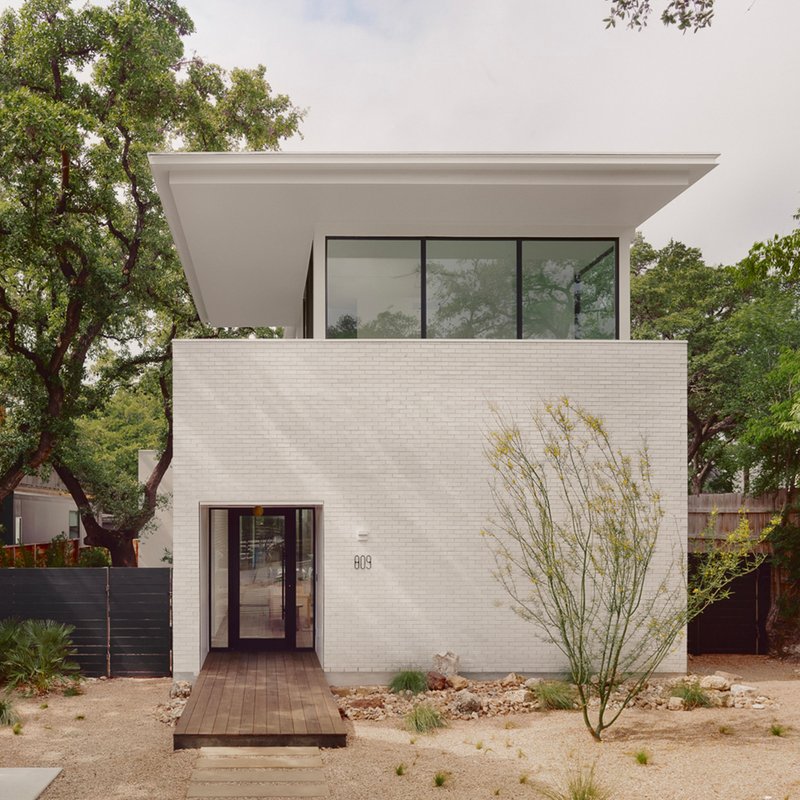 Street facade with white brick and recessed glazed entry flanked by a desert landscape with grasses