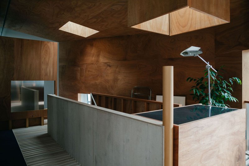 Upper level with plywood walls and ceiling, concrete balustrade, and skylights above a planted interior courtyard