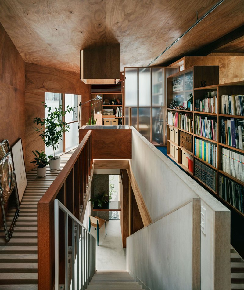 Upper mezzanine with bookshelves and translucent panels overlooking the lower dining level through a plywood ceiling void