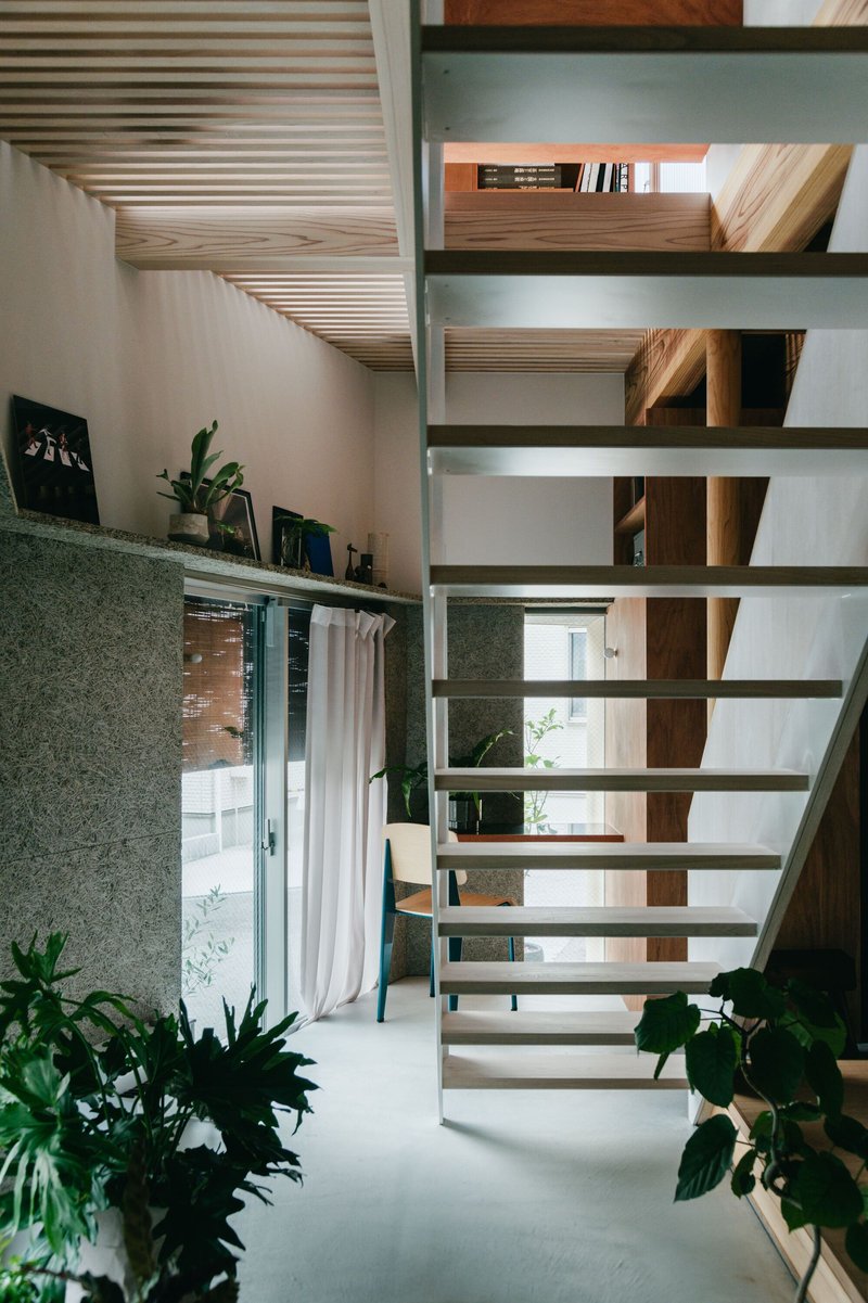 Open-tread timber staircase ascending past textured green wall panels and potted plants
