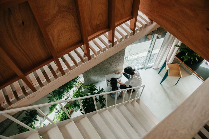 View down white timber stairs toward workspace with person seated at desk and surrounding greenery