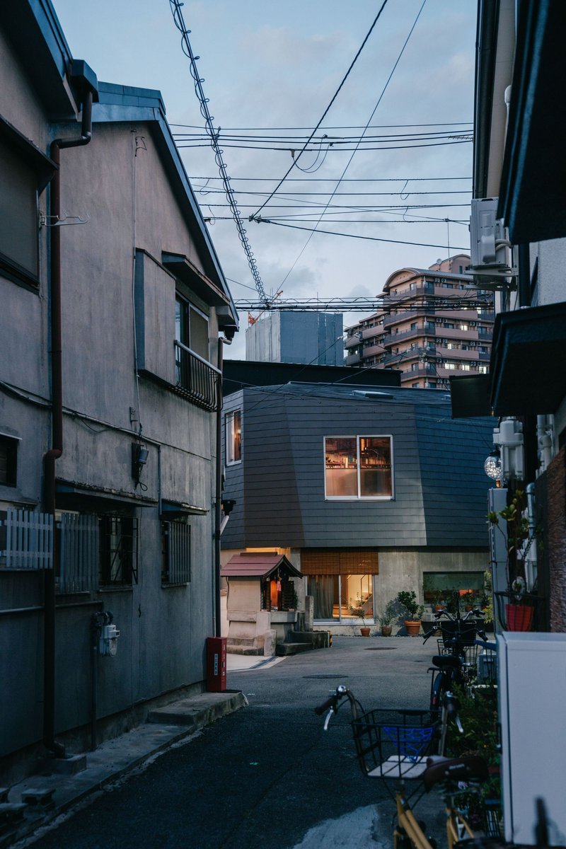 Charcoal-clad volume in a narrow urban lane at dusk with overhead power lines
