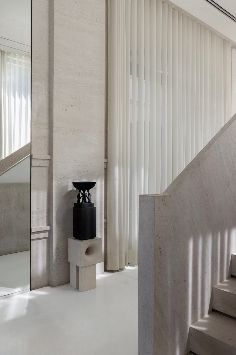 Interior view showing stone walls, vertical curtains, and a black sculpture on a pale plinth