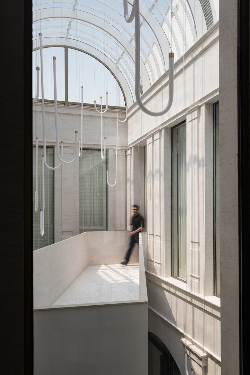 Interior courtyard with curved glass roof, linear pendant lights, and a figure crossing the bridge