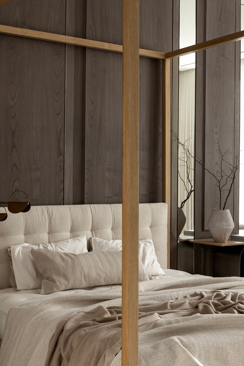 Bedroom with timber-framed canopy bed against dark wood paneled walls and sheer curtains