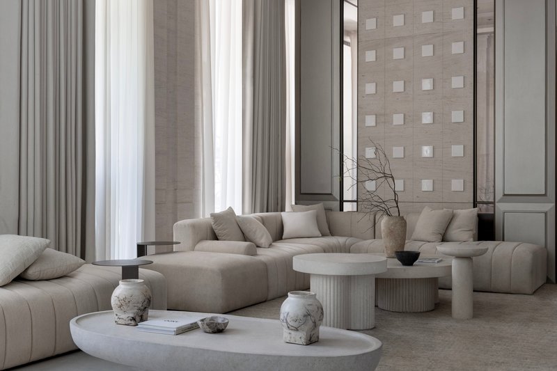 Double-height living room with floor-to-ceiling curtains and grey upholstered seating around circular tables