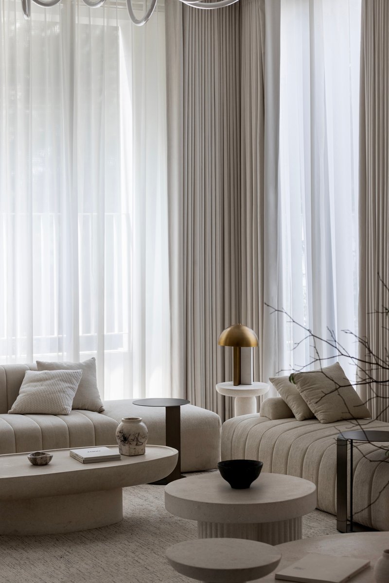 Living area with layered sheer curtains filtering daylight over modular seating and fluted stone tables