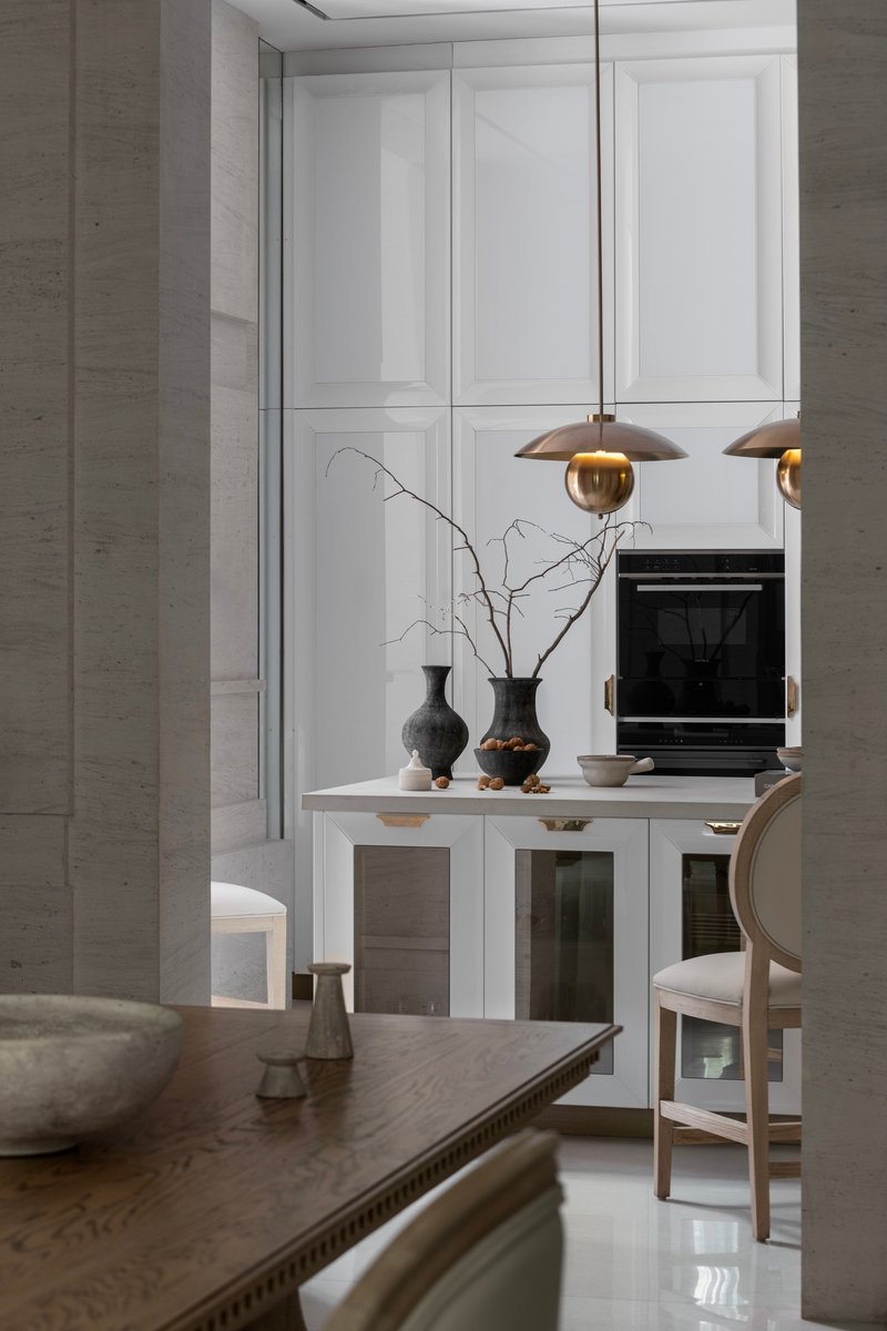Kitchen island with brass pendant lights and decorative branches against white paneled cabinetry
