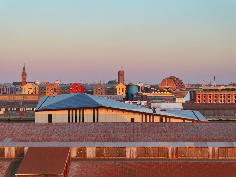 Roofscape perspective with the solar panel roof volume emerging above brick warehouse rooftops at twilight