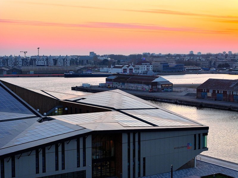Rooftop view of the angled photovoltaic panels and glazed facade overlooking the waterfront at sunset