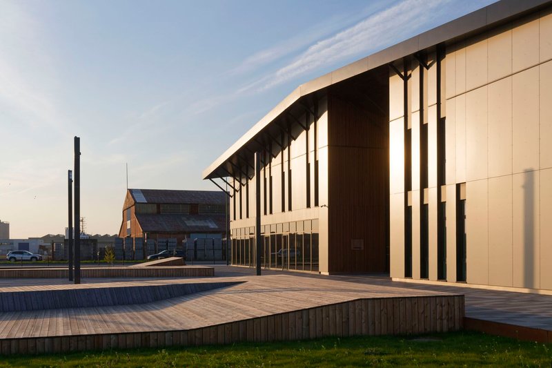 Timber-decked plaza in front of the slatted facade with deep overhang at golden hour