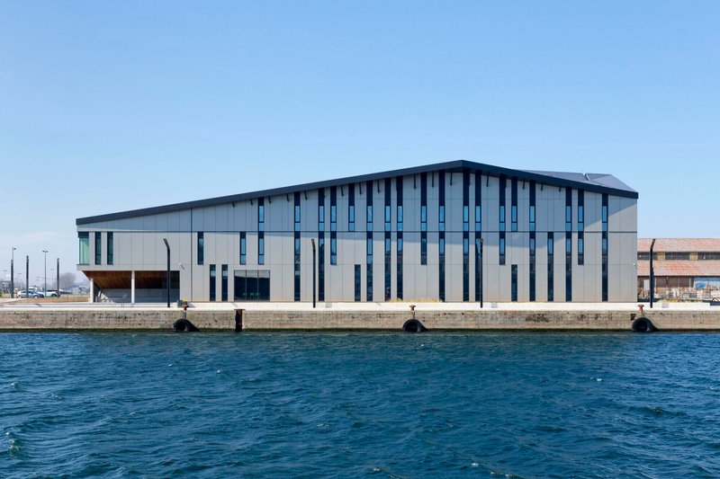 Waterside elevation with vertical window slots and metal cladding seen from across the harbor