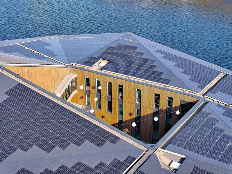 Aerial view of courtyard with solar panel roof and timber-clad building above water
