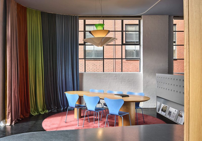 Meeting area framed by multicolored curtains with tiered pendant light hanging over timber table