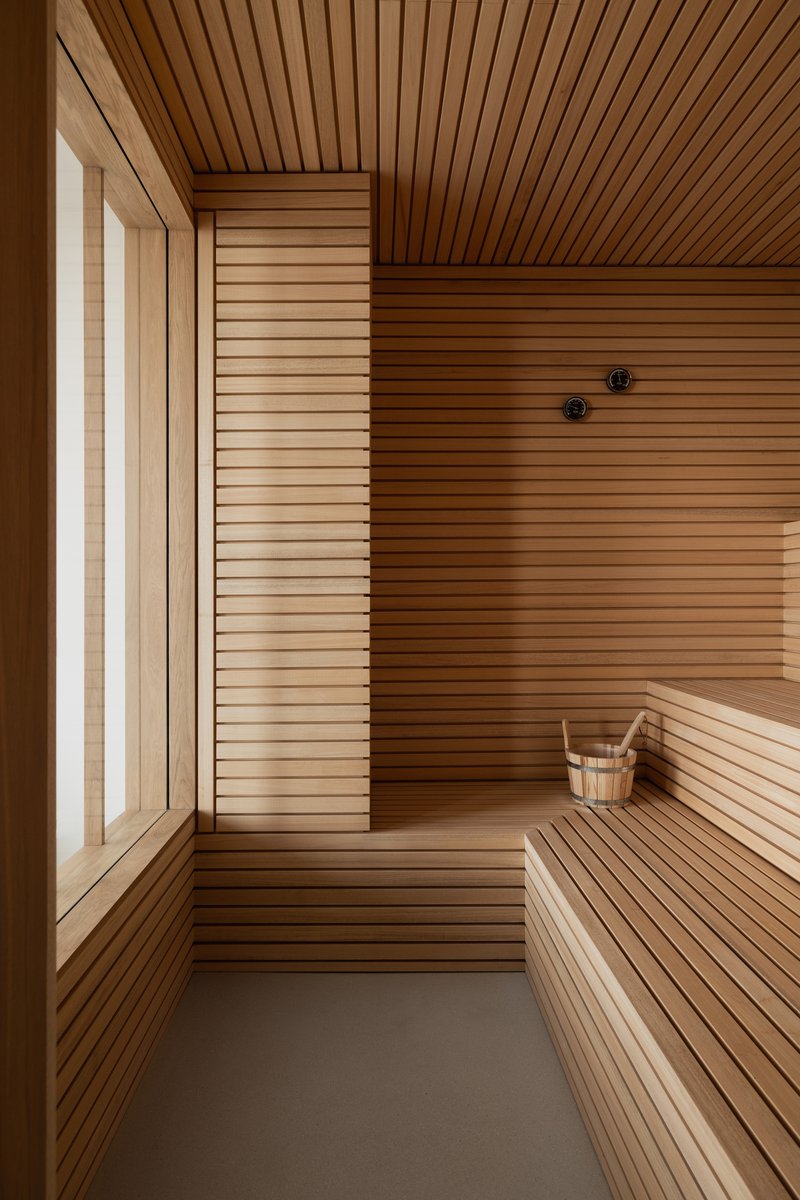 Sauna interior with horizontal timber slat walls, benches, and a wooden bucket on the floor