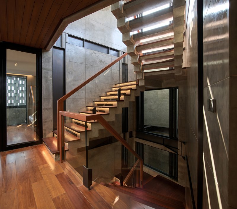 Open timber staircase rising through a double-height volume with slotted skylight and wood ceiling