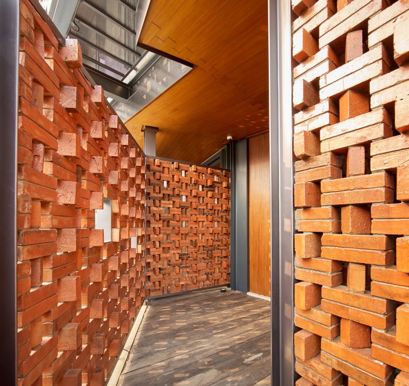 Narrow passageway lined with textured brick walls in a basket-weave pattern beneath a timber ceiling and skylight
