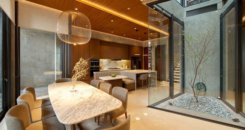 Dining area with marble table and glass-enclosed courtyard featuring a tree on white pebbles