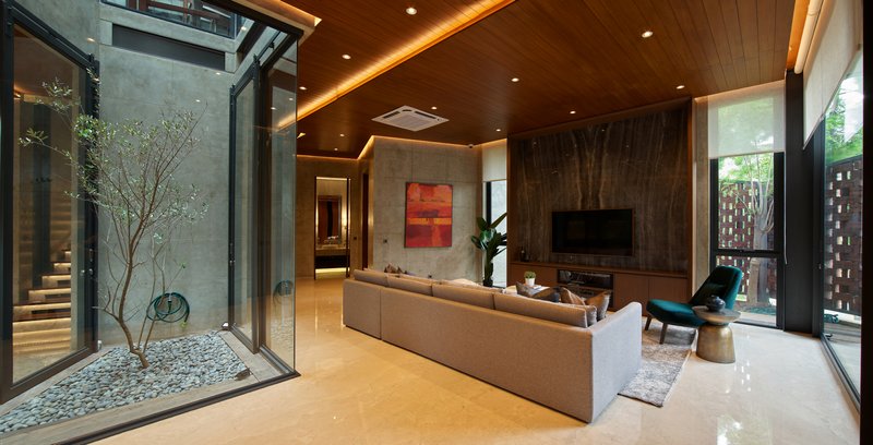 Living space with timber ceiling opening to two glazed courtyards with trees and stone flooring