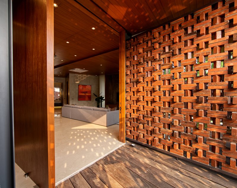 Entry threshold with pivoting perforated brick screen opening to living space beyond timber door frame