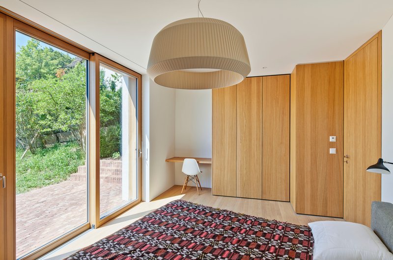 Bedroom with sliding glass door opening to a brick terrace and timber storage wall