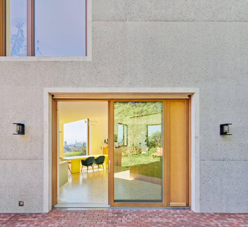 Timber-framed sliding glass doors with wall-mounted sconces flanking the entrance on brick paving