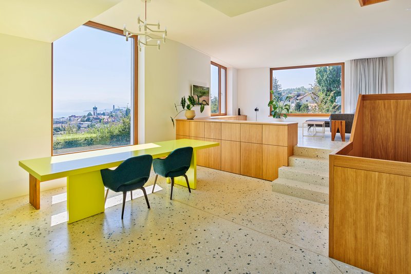 Split-level interior with terrazzo flooring, timber cabinetry, chartreuse table, and window framing distant cityscape