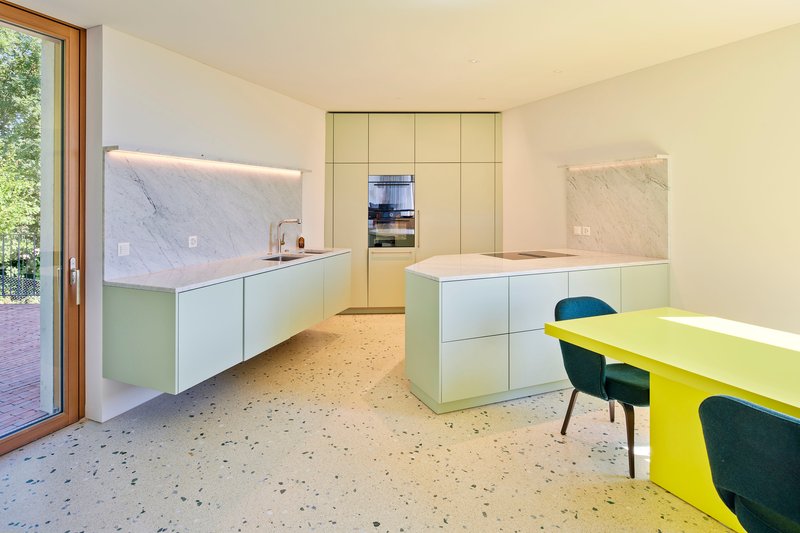 Kitchen with floating pale green cabinetry, marble backsplash, terrazzo floor, and chartreuse dining table